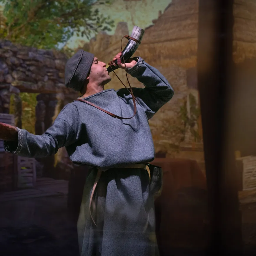A man in anglo saxon attire blows a horn to the sky