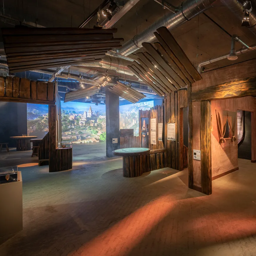 A room with wooden structures, on the back of the room is a large projection of an anglo saxon town