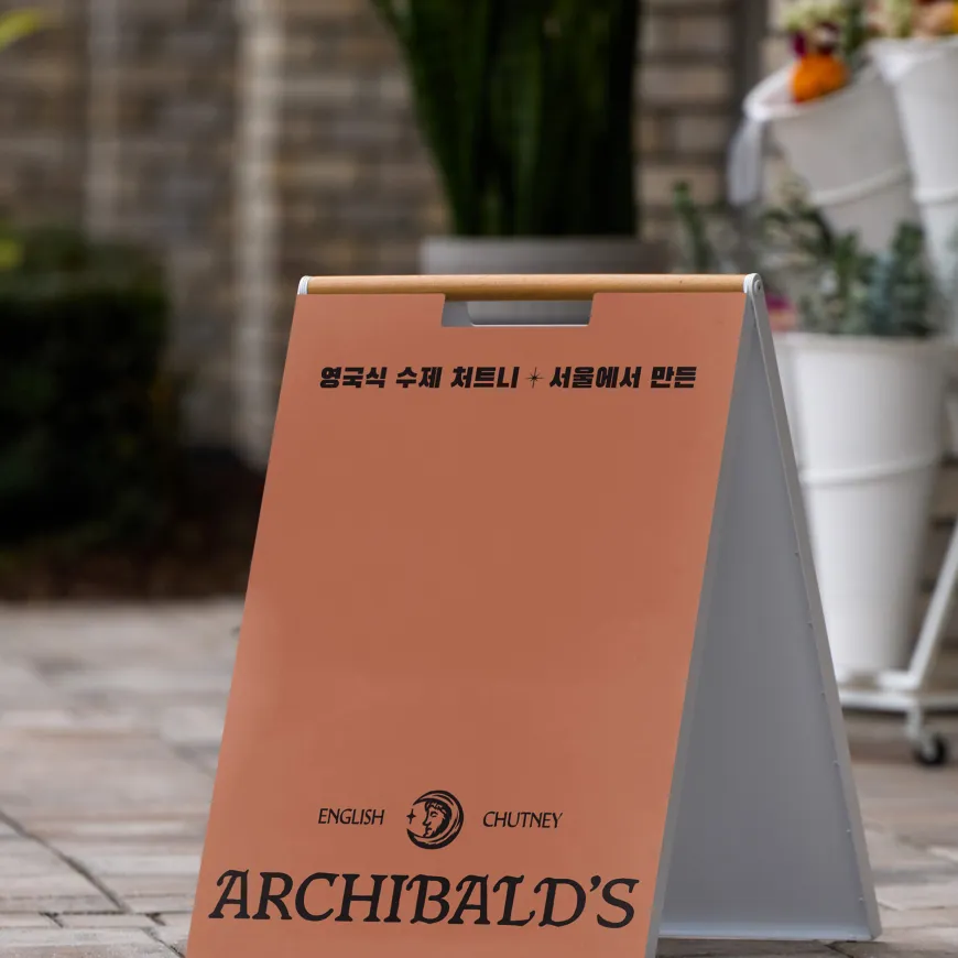 A-frame sidewalk sign with Archibald’s branding displayed outdoors against a blurred garden backdrop