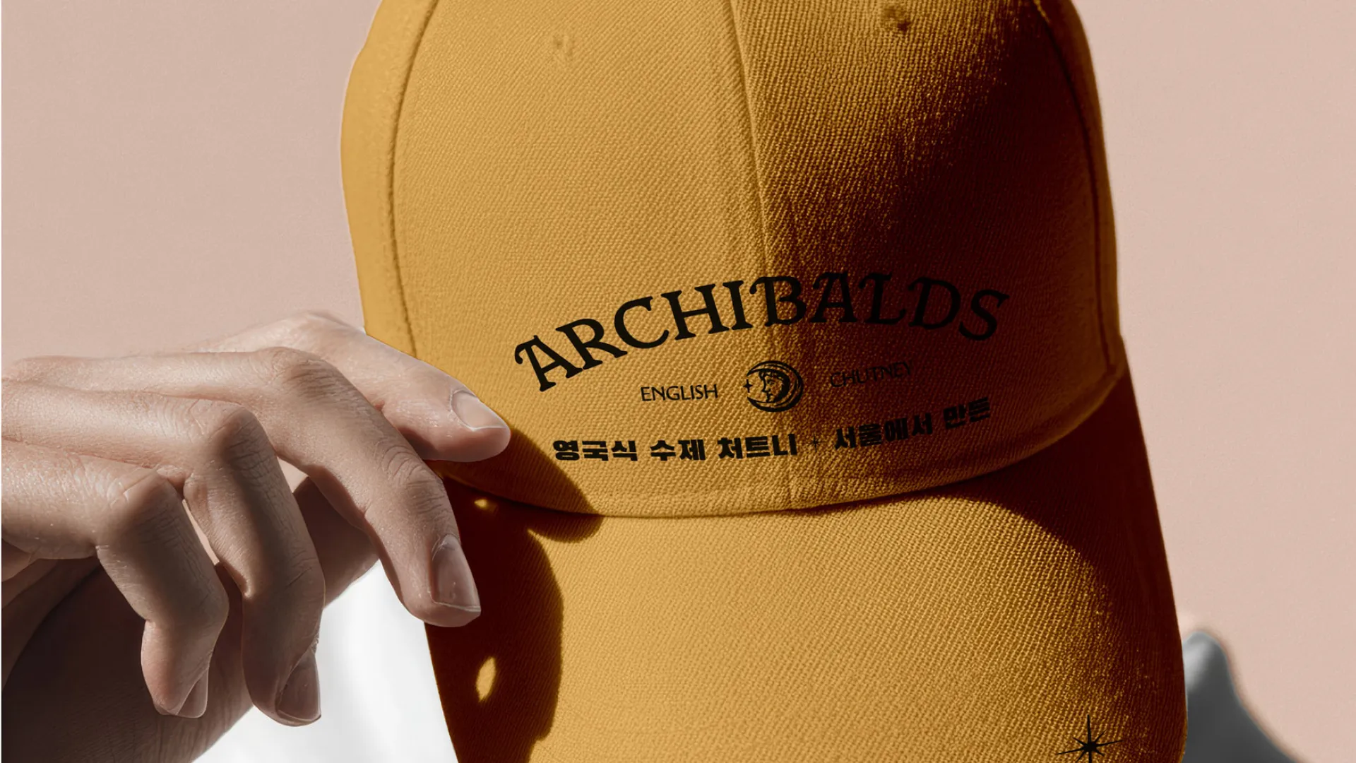 Person adjusting a mustard-coloured Archibald’s branded cap in soft natural light