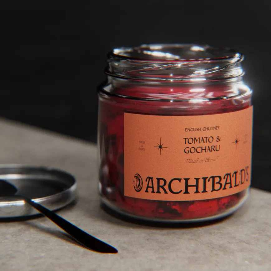 Glass jar of Archibald’s Tomato & Gocharu chutney beside its lid and a small spoon