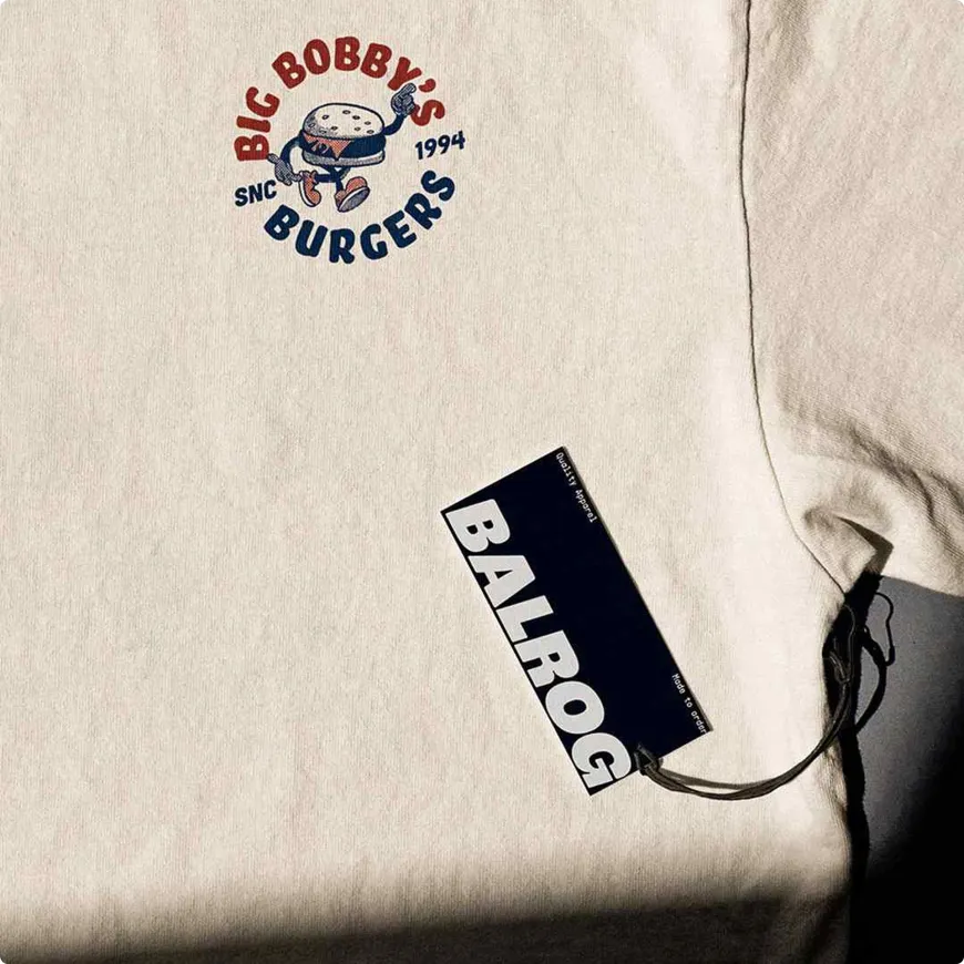 Cream t-shirt with Big Bobby's burgers illustration and Balrog clothing tag