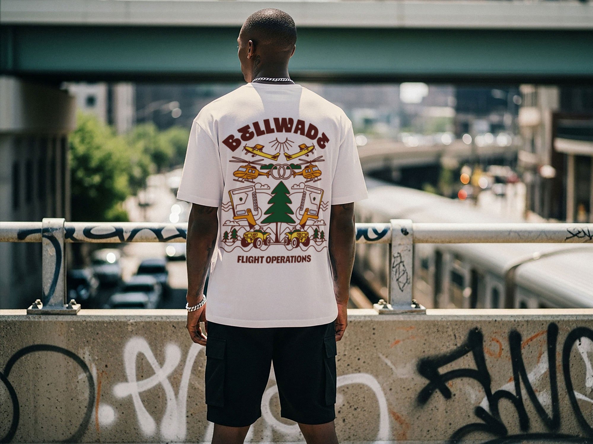 A man standing on a bridge facing away from camera wearing a white t-shirt