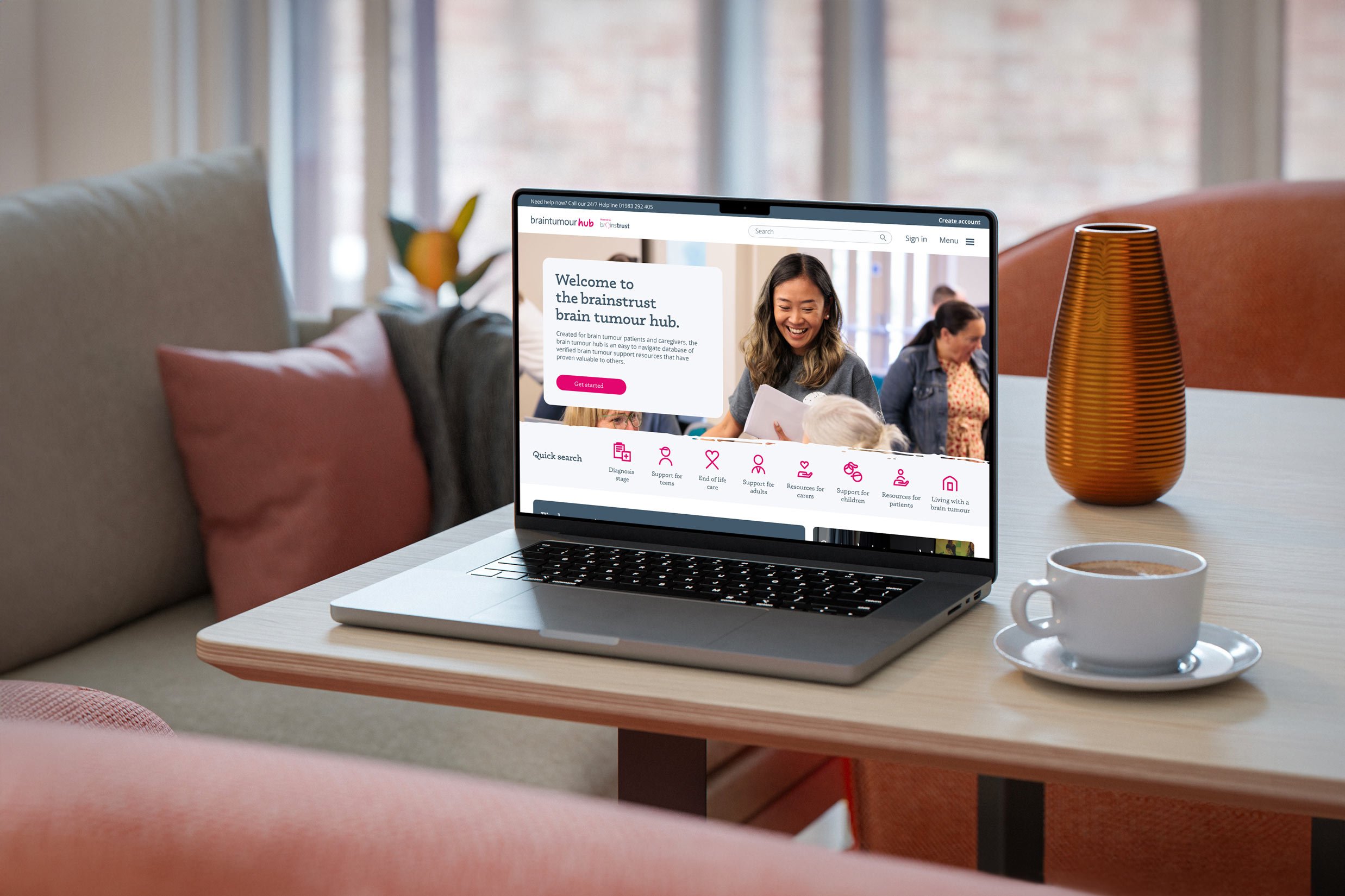 Laptop displaying the Brain Tumour Hub on a coffee table with cup and saucer.