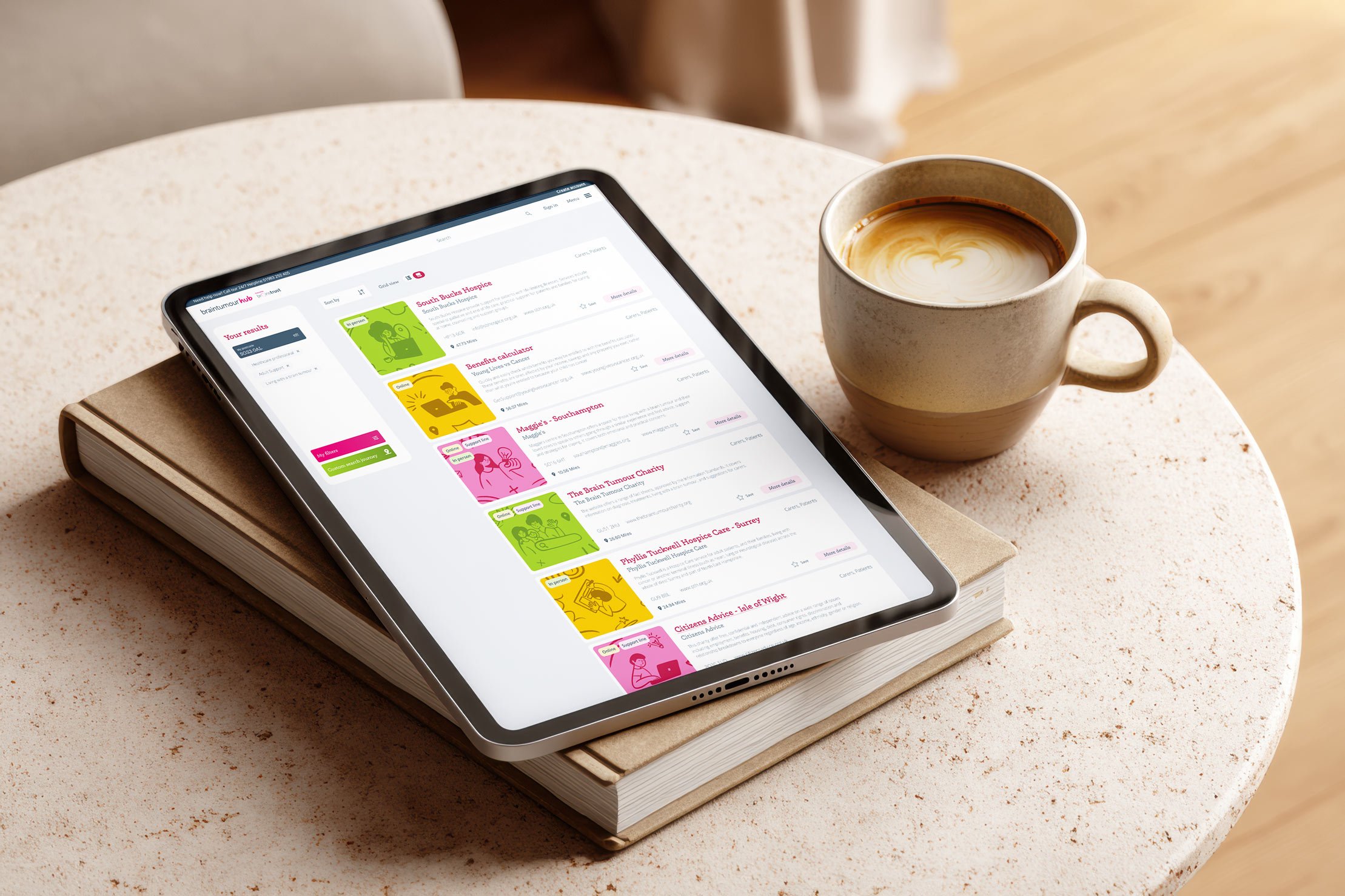 Tablet mockup of Brain Tumour Hub resources search page, laid on a coffee table and book.
