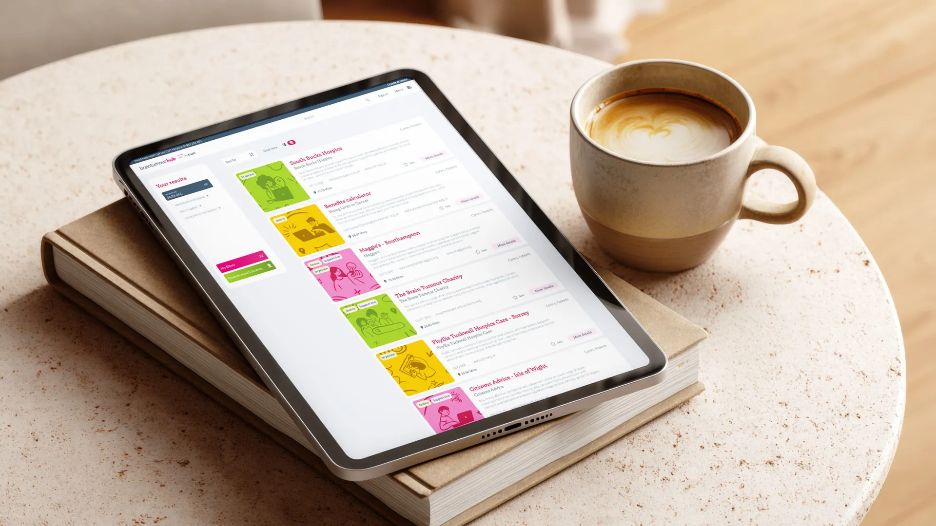 Tablet mockup of Brain Tumour Hub resources search page, laid on a coffee table and book.