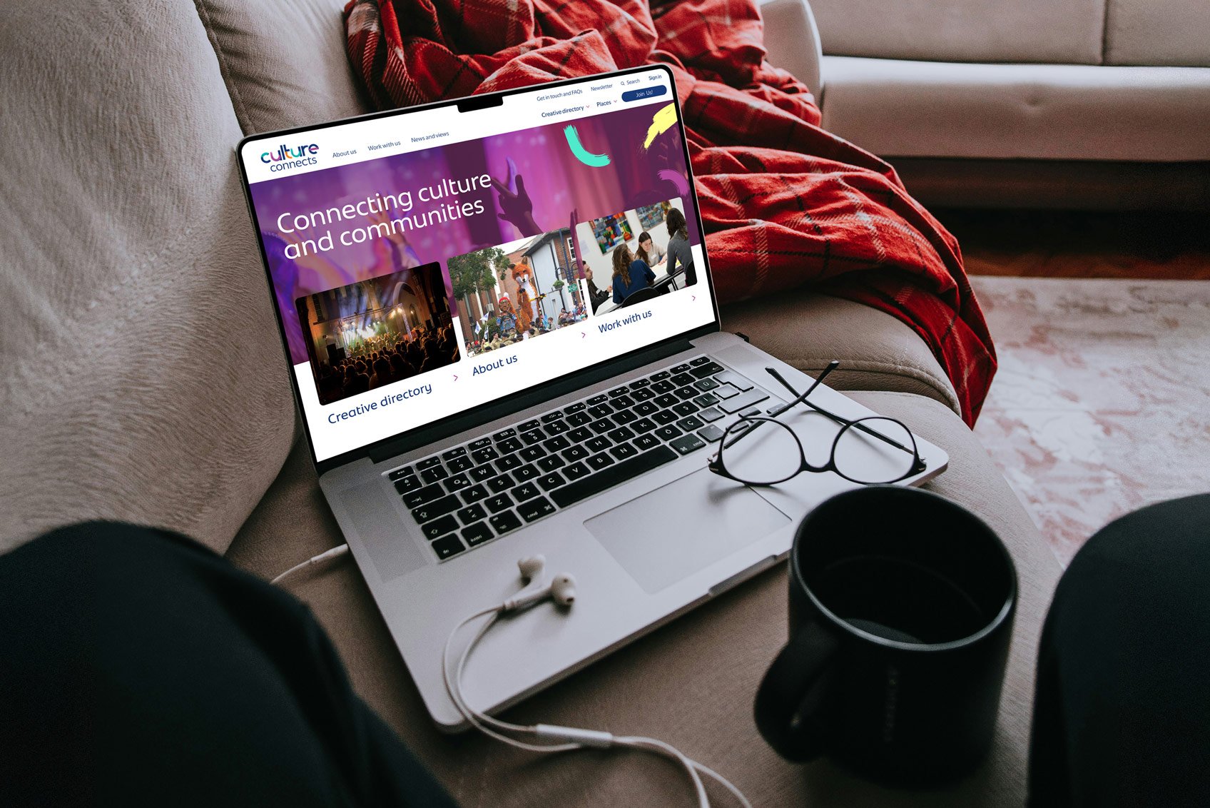 Culture connects website on laptop, on a sofa with headphones.
