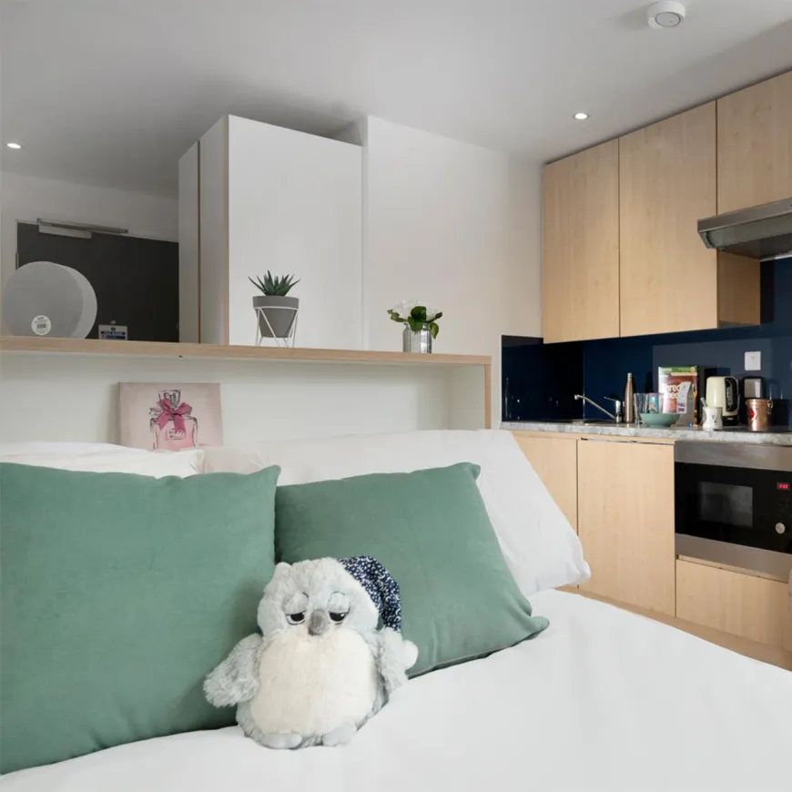 Close up of double bed backing onto studio kitchen living space