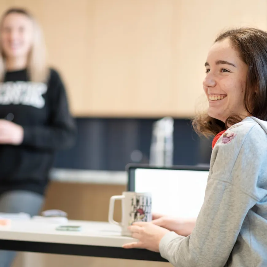 Happy girl smiling and holding a mug at her desk