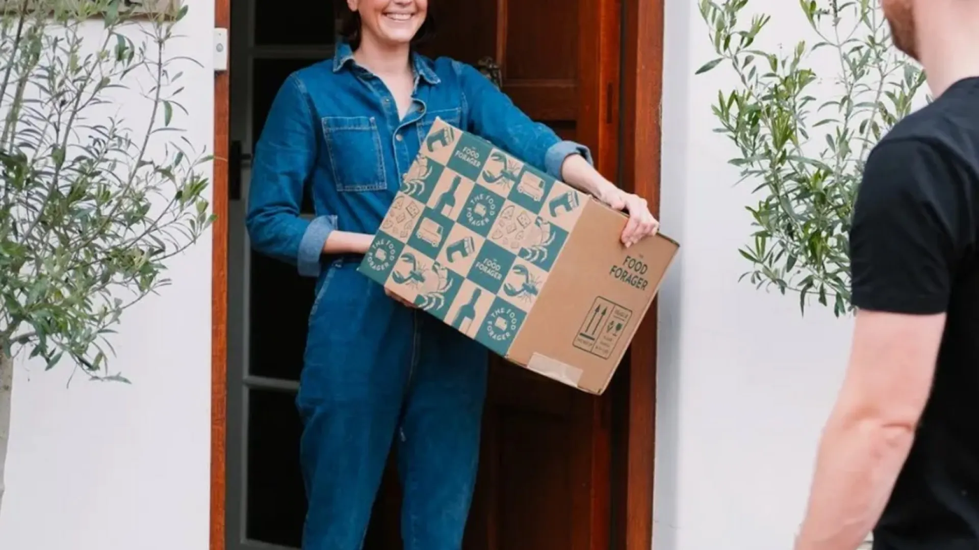 a woman at her front door receives a delivery of a food forager box