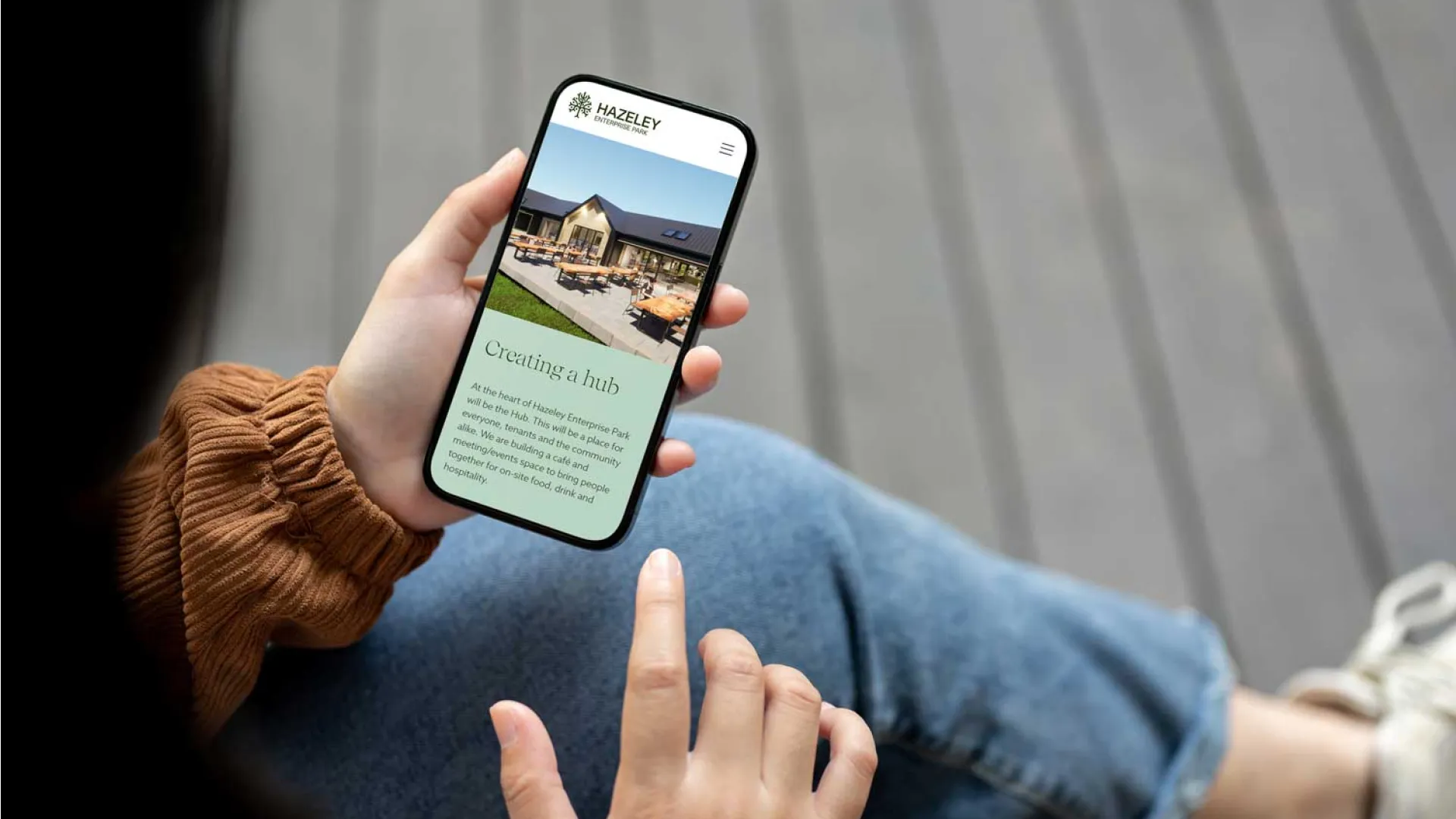 Person using a smartphone to view the Hazeley Enterprise Park website highlighting plans for a community hub and event space