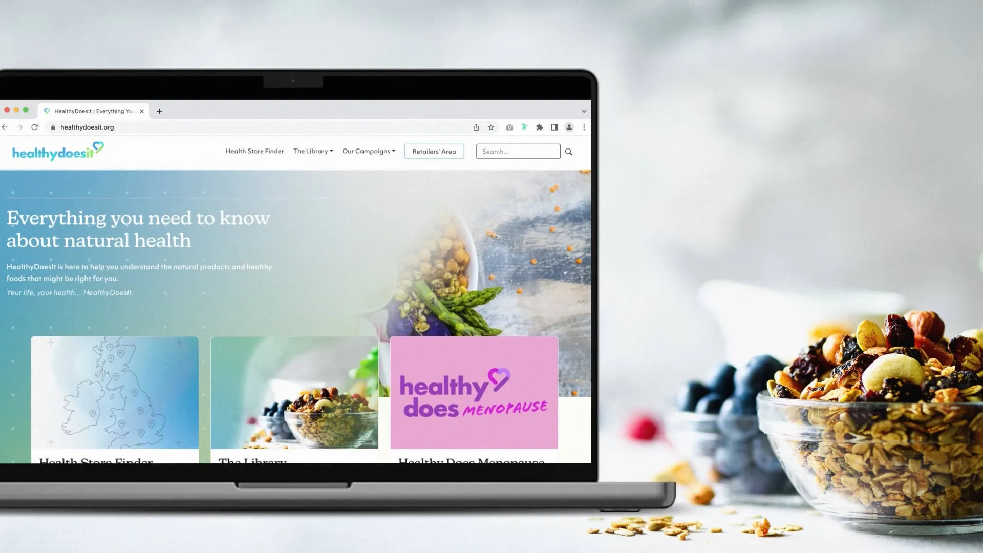 Healthy does it laptop mockup on home page, next to some bowls of fruit and nuts.