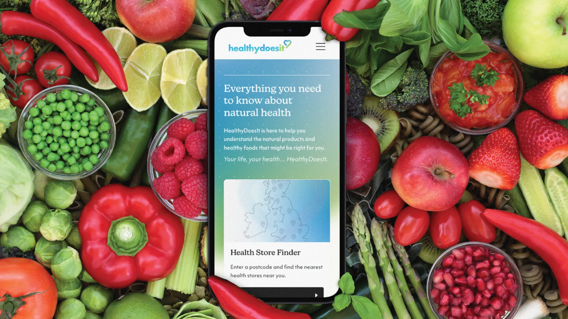 Mobile phone open on healthy does it website, laid in a bed of green and red fruit and vegetables.