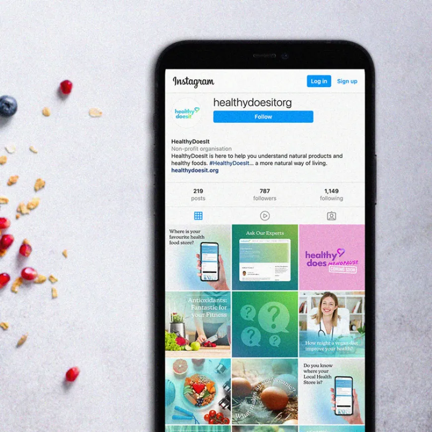 Mobile phone mockup of Instagram page for healthy does it, next to a bowl of yogurt, fruit and nuts.