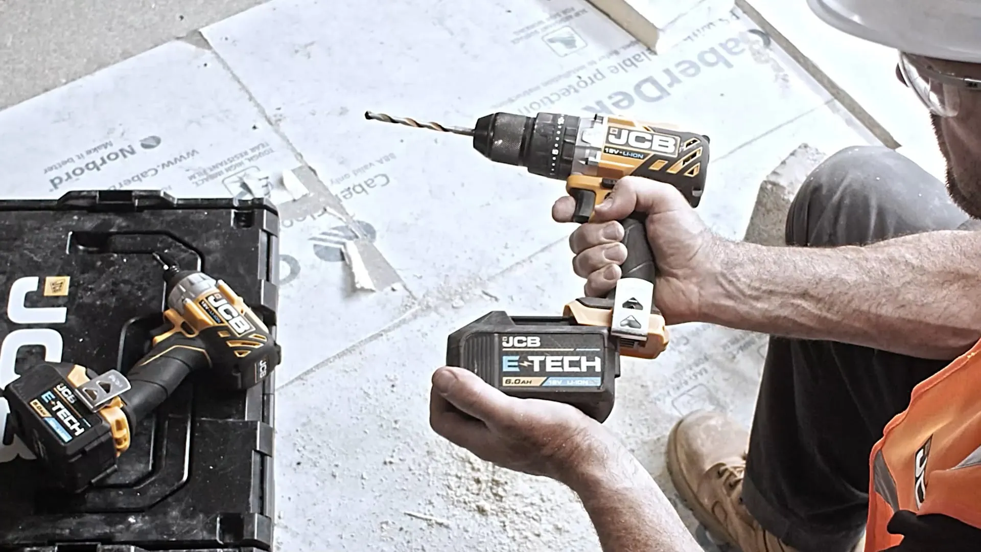 a man in orange hi vis changes the batter on a jcb drill