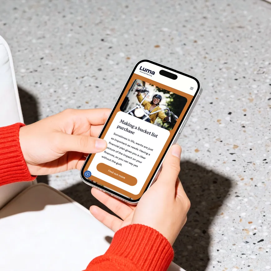 Person holding a smartphone displaying the Luma Financial Planning website with an article about making a bucket list purchase