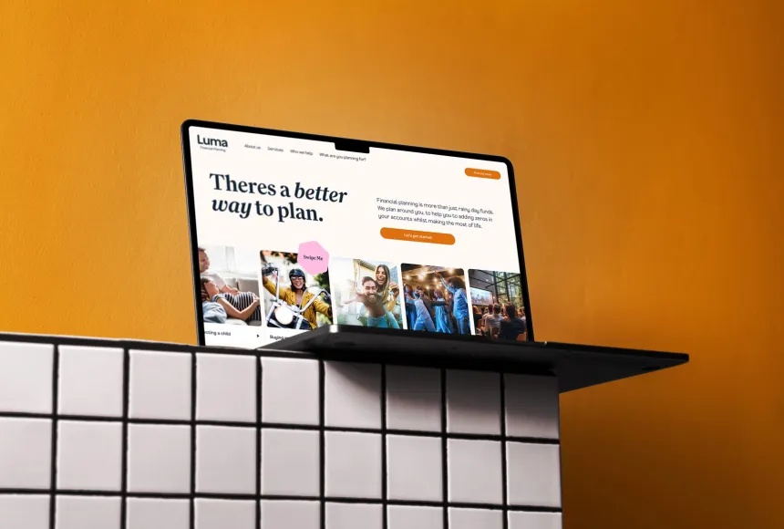 Laptop perched on the edge of a white tiled shelf against an orange background.