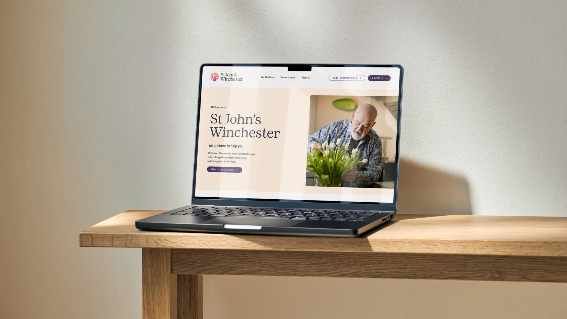 A laptop displaying the St John’s Winchester website on a wooden table.