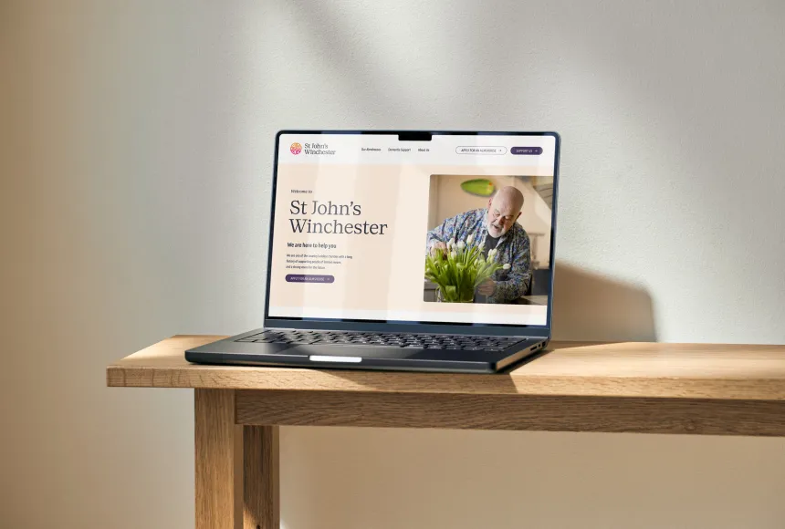 A laptop displaying the St John’s Winchester website on a wooden table.
