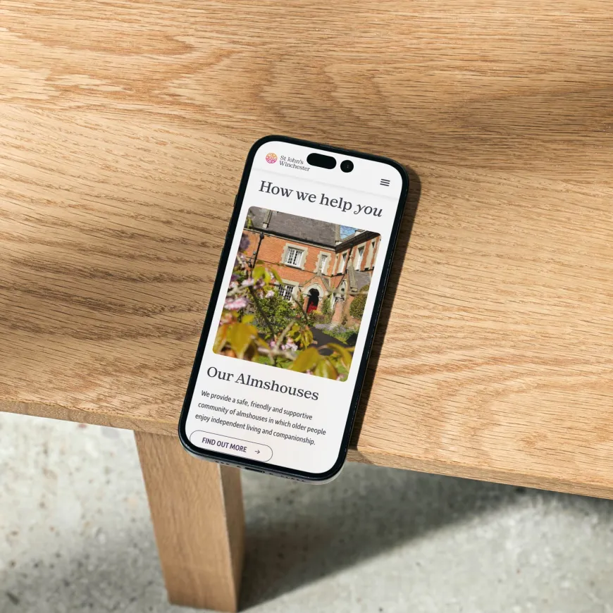 A smartphone displaying the St John’s Winchester website on a wooden table.