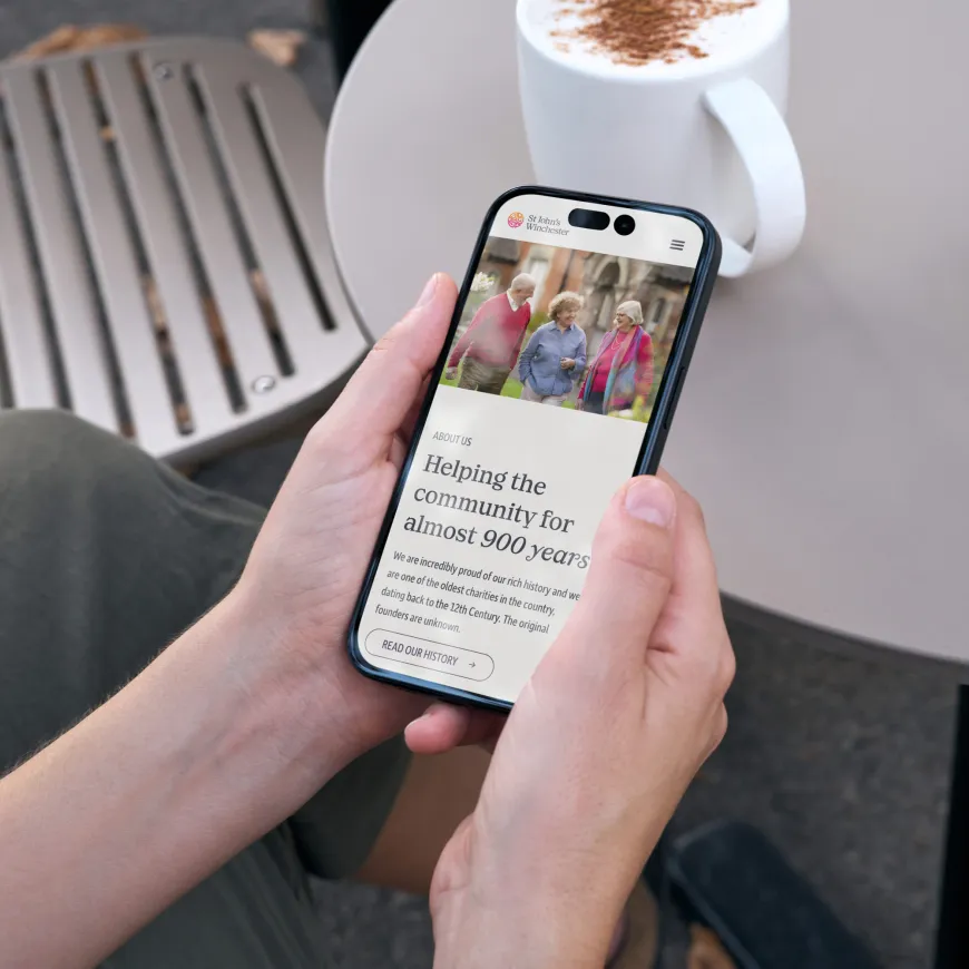 A person holding a smartphone displaying the St John’s Winchester website.