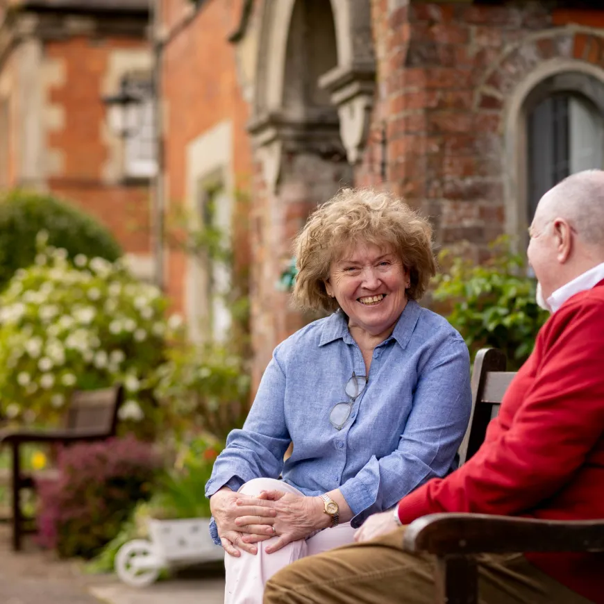 Two older adults sitting and chatting in a landscaped courtyard.
