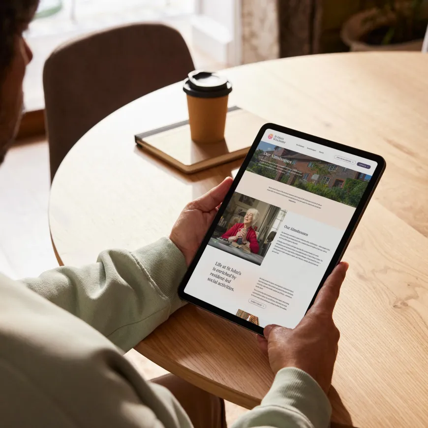 A person viewing the St John’s Winchester website on a tablet at a wooden table.