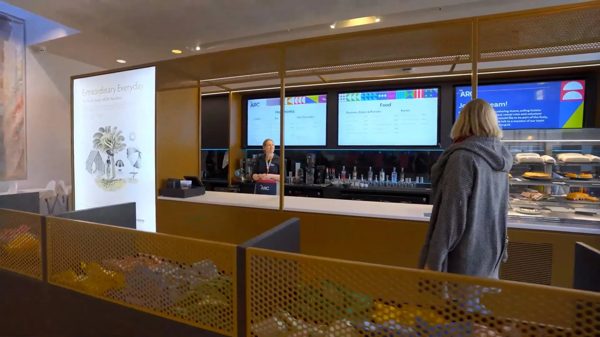 A lady in a grey coat approaching the counter of the arc cafe