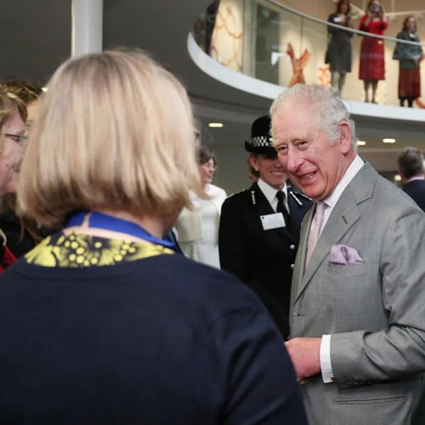 An image of King Charles in a grey suit talking to a woman with short blonde hair