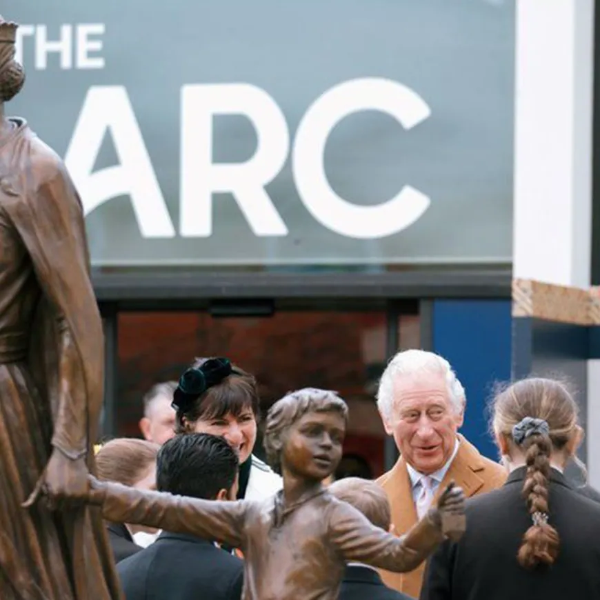 King charled standing next to a bronze statue under signage reading 'The Arc'