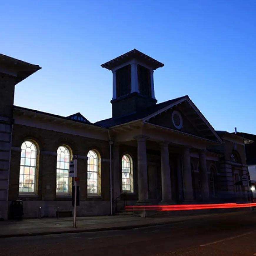 Exterior image of a building as the sun sets, in the foreground is a light streak in red