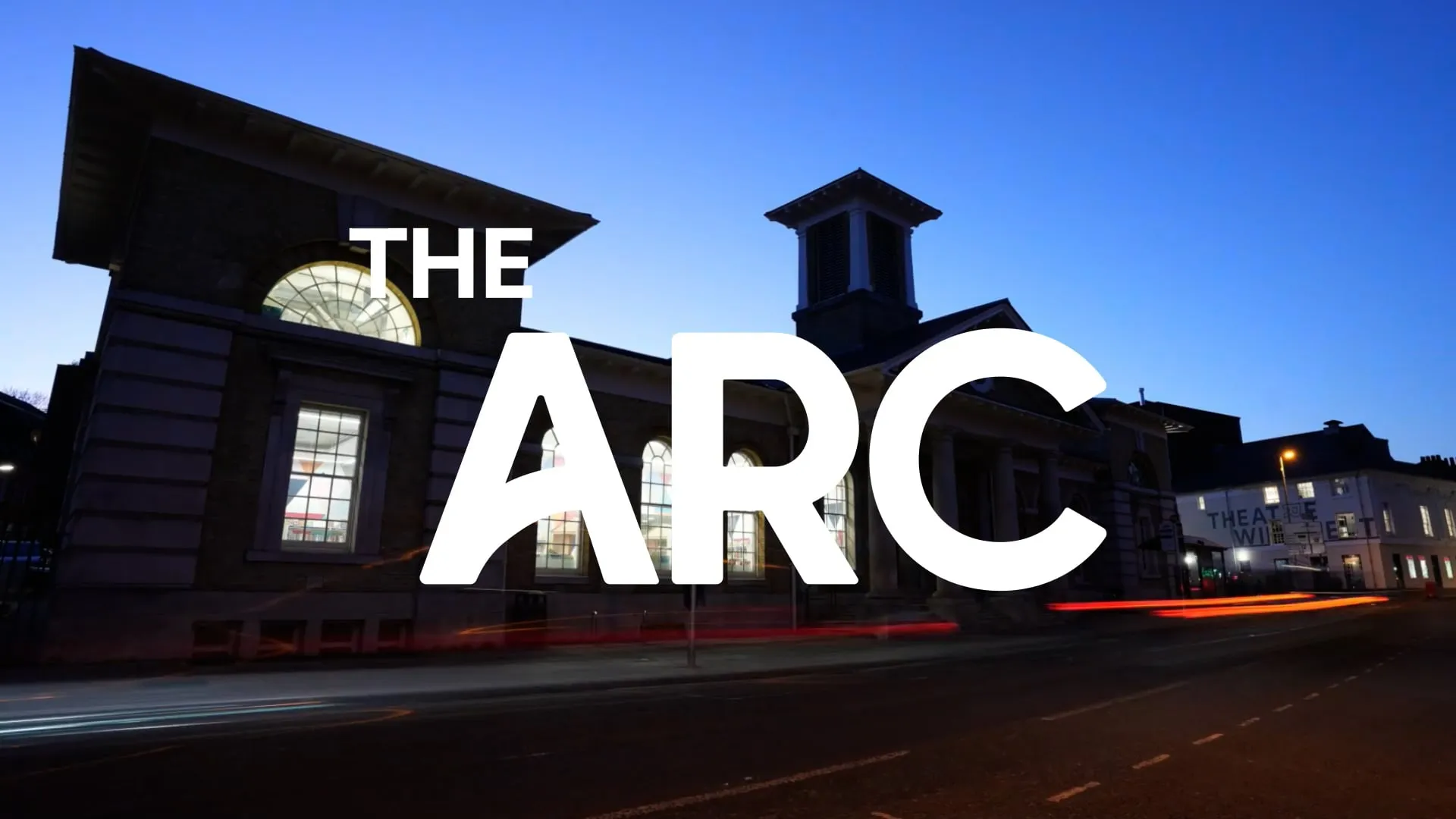 The Arc written in white in front of a grand building at sunset