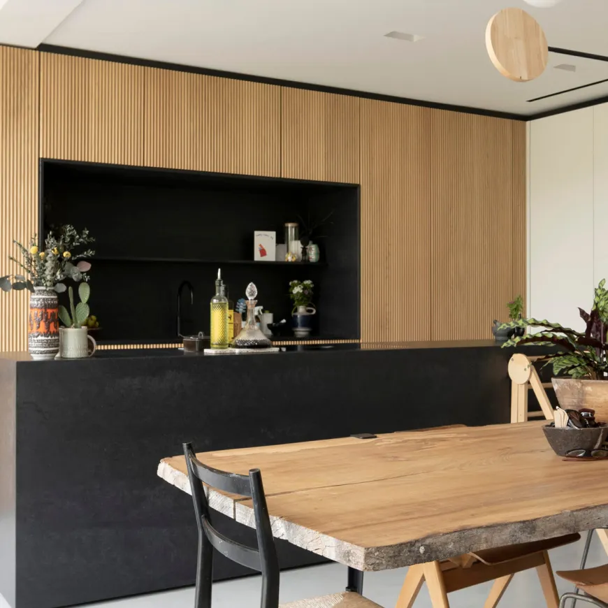 Modern kitchen with wood slat cabinetry, black countertops, and a rustic dining table