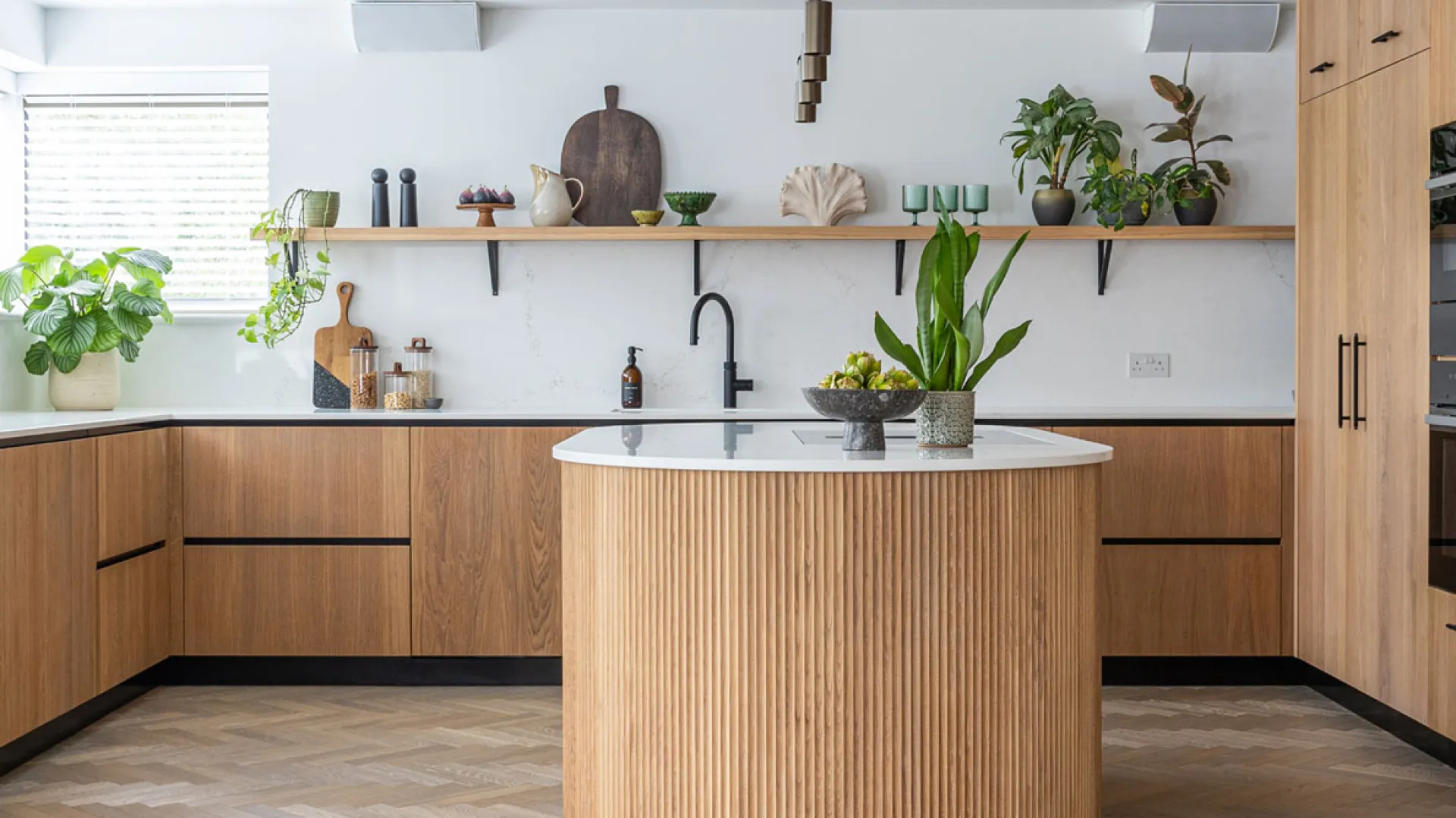 Contemporary kitchen with wood cabinetry and a curved fluted island
