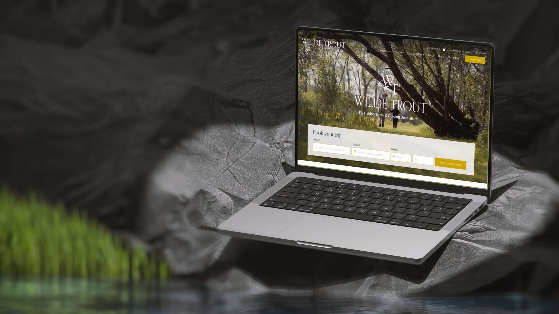 Laptop mockup of Wilde Trout homepage on a rock next to a stream of water.