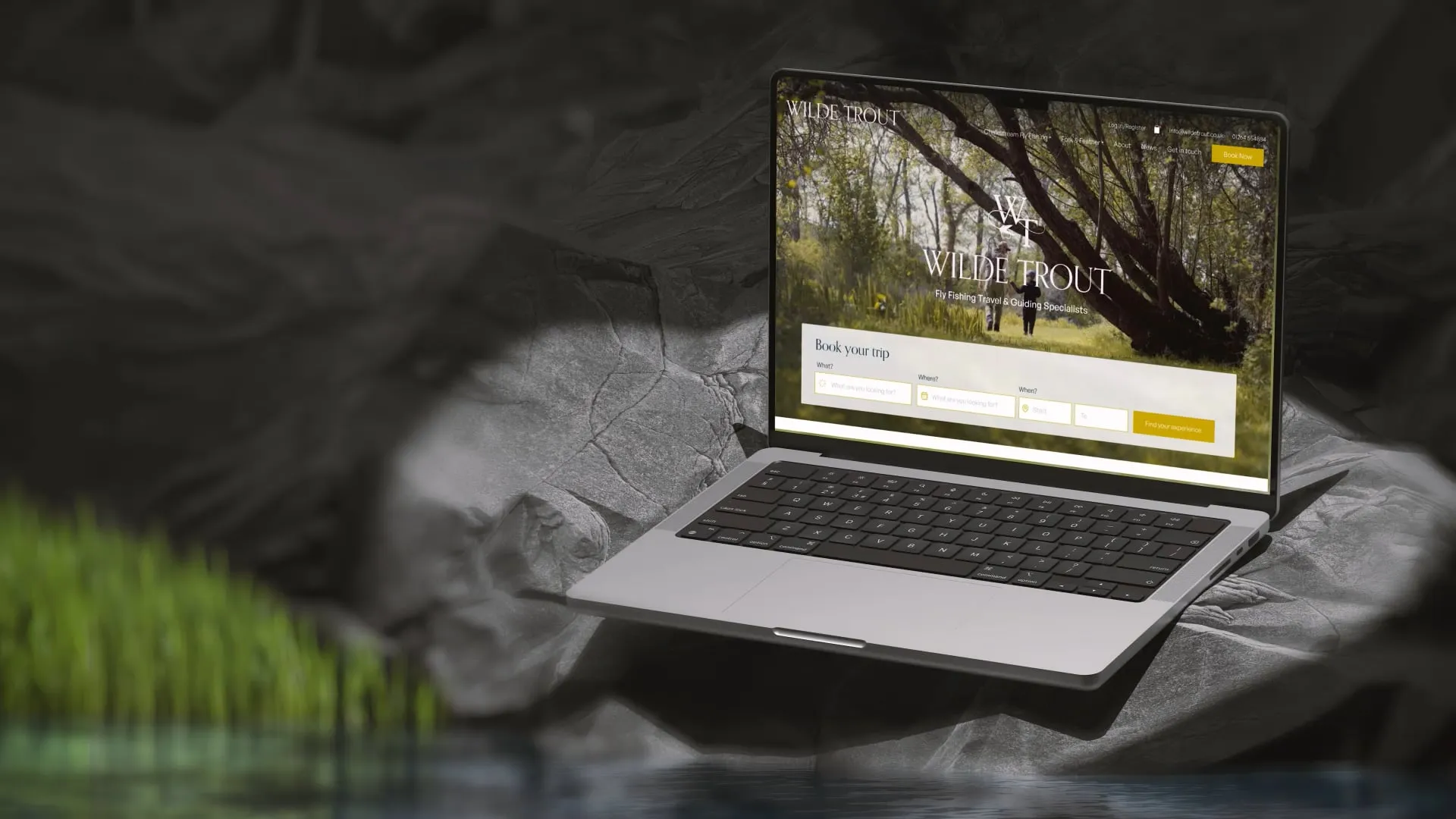 Laptop mockup of Wilde Trout homepage on a rock next to a stream of water.