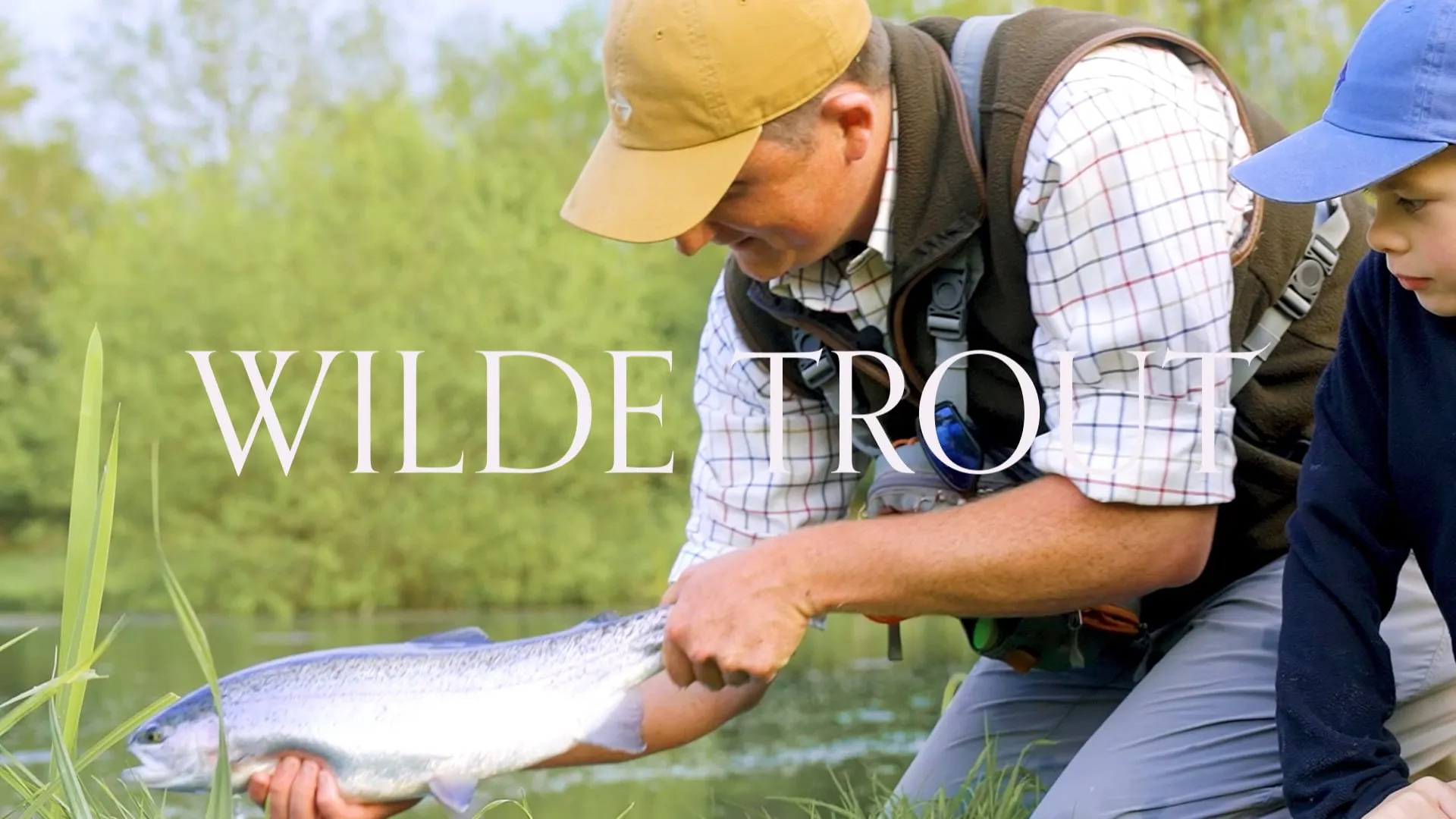 Photo of man and child fishing, man holding large trout. With Wilde Trout written over top of image.