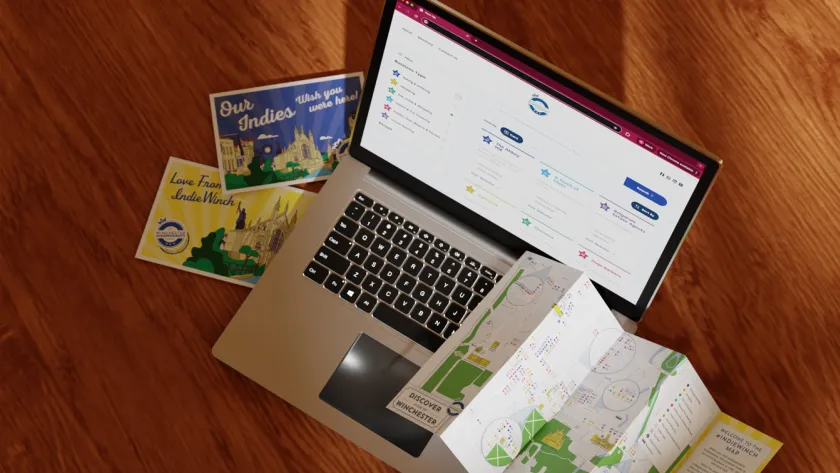 Laptop mockup, postcards and Winchester map laid out on a wooden surface.